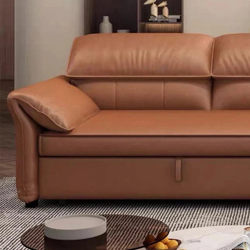 Close-up of  tan brown sofa bed showing padded arm, stitched back panels, storage pull strap, and cushioned seating